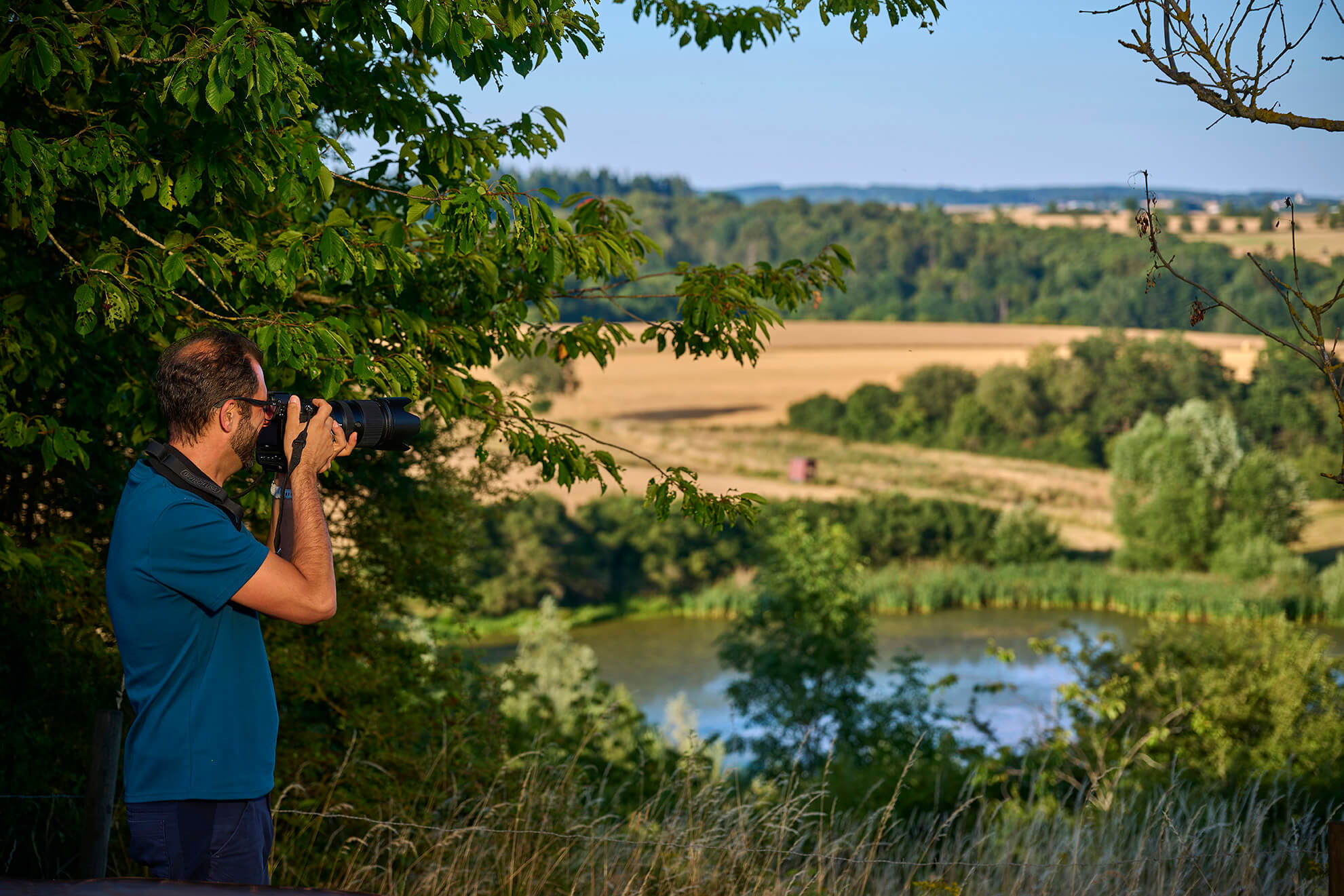 Wanderer mit Kamera beim Blick über einen Weiher und die Landschaft bei Strohn in der Vulkaneifel