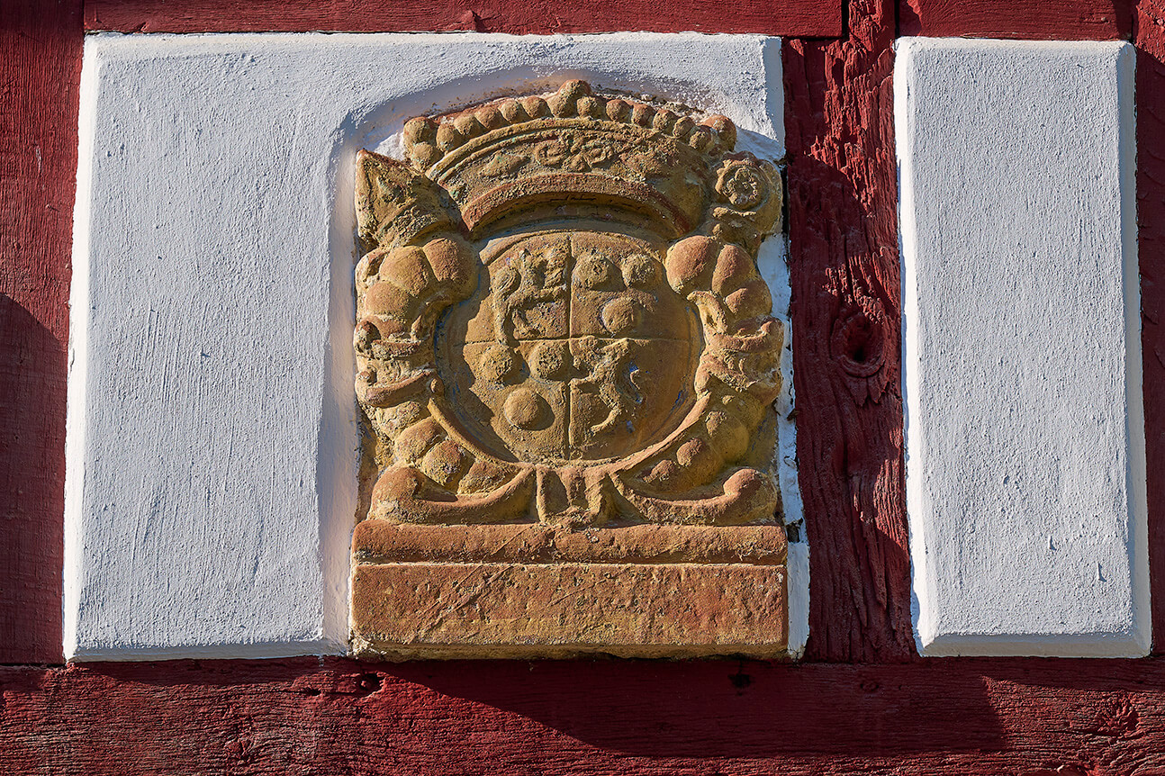Historisches steinernes Wappen an einer rot weiß gestalteten Fachwerkfassade in Strohn