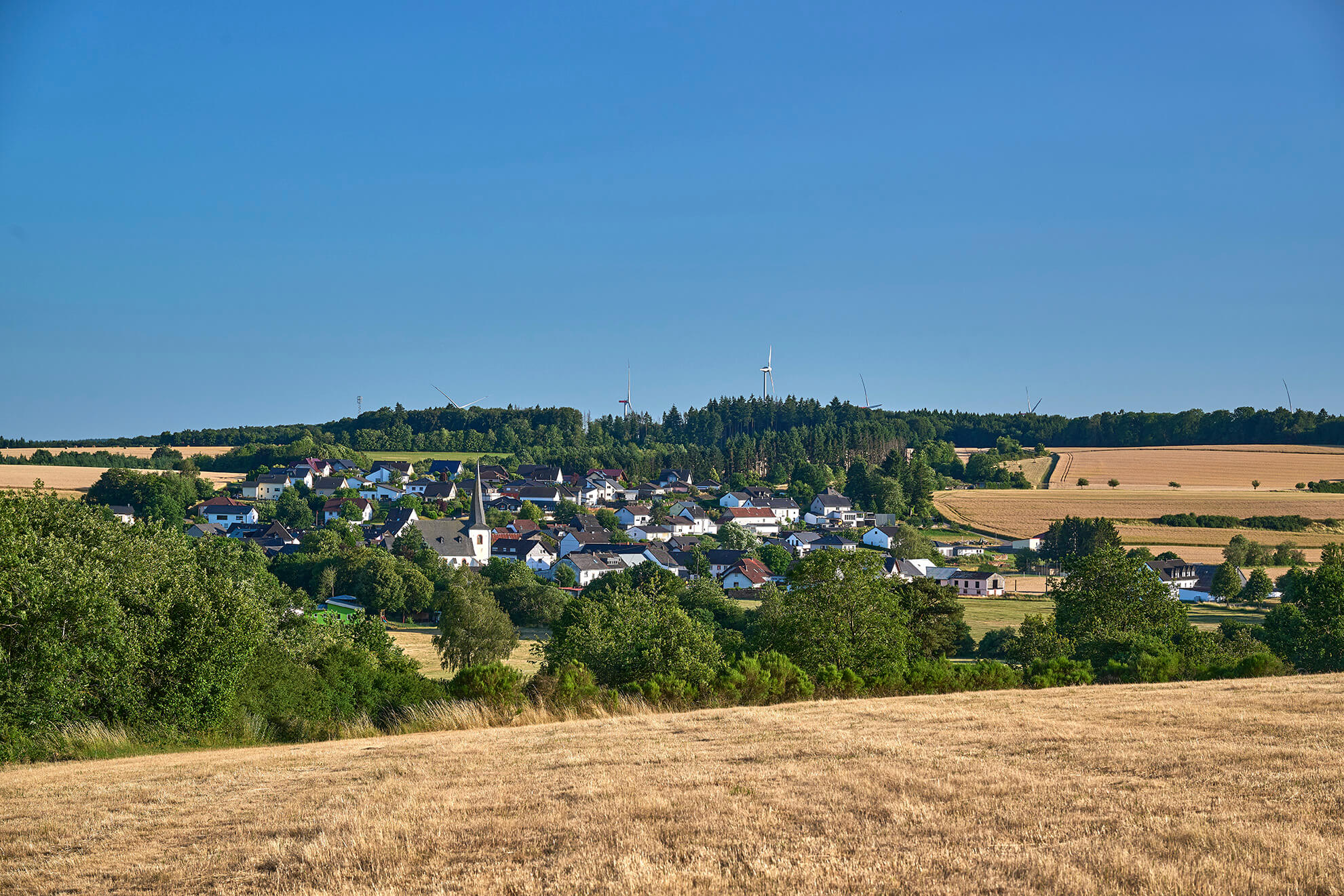 Weitblick über Strohn mit Kirche, Feldern und bewaldeter Landschaft der Vulkaneifel
