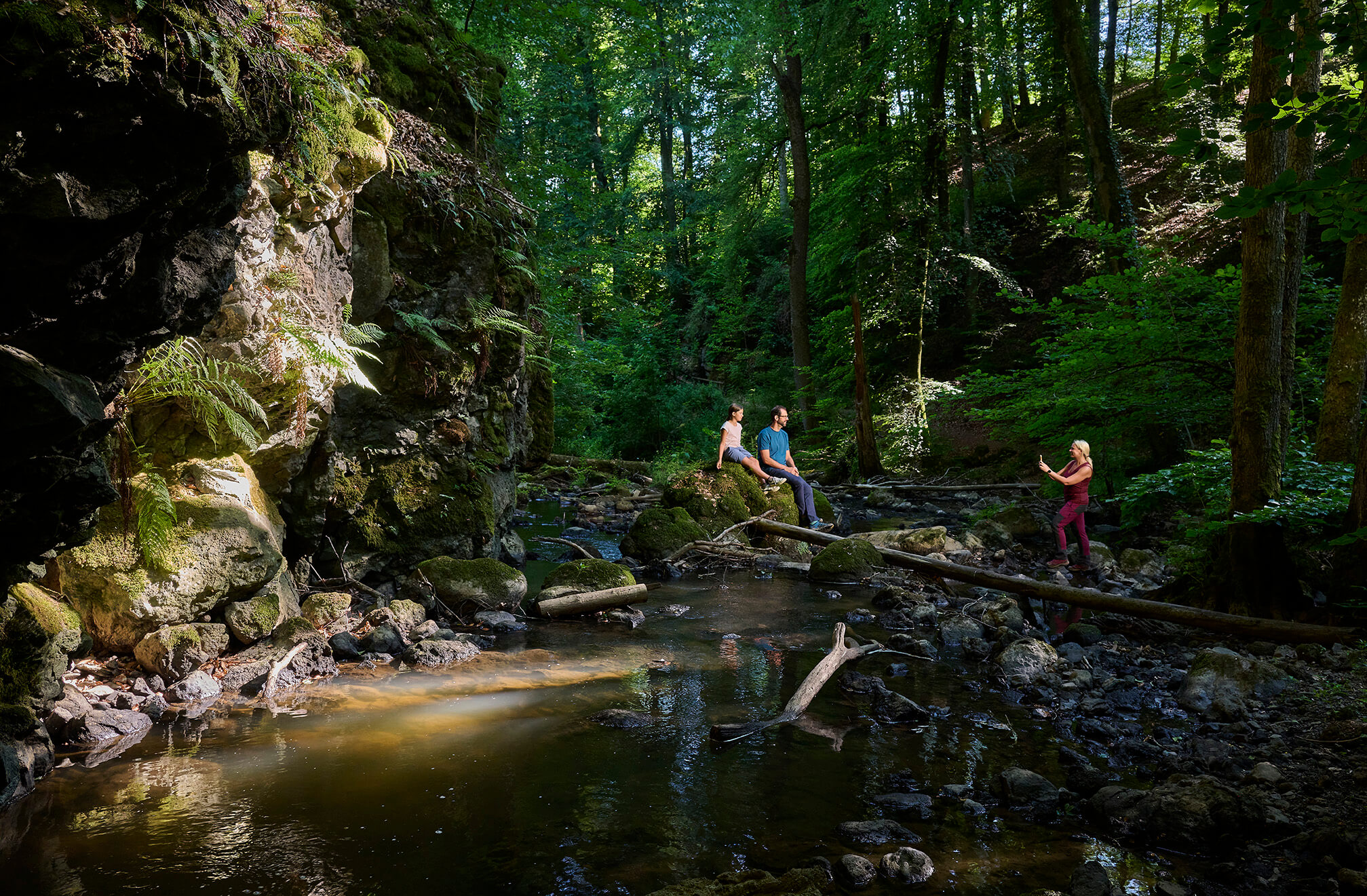 Wanderer in einem bewaldeten Bachtal mit Felsen bei Strohn in der Vulkaneifel
