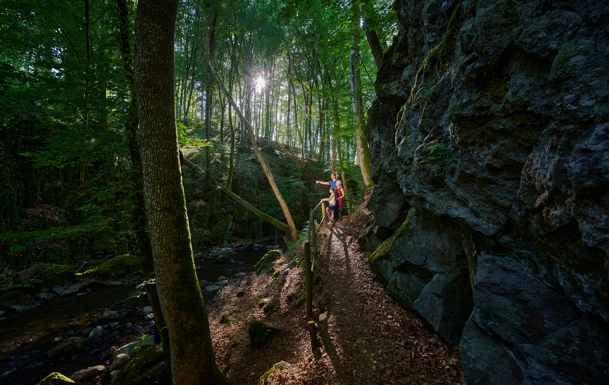 Wanderer auf einem schmalen Pfad zwischen Felsen und Bach bei Strohn in der Vulkaneifel