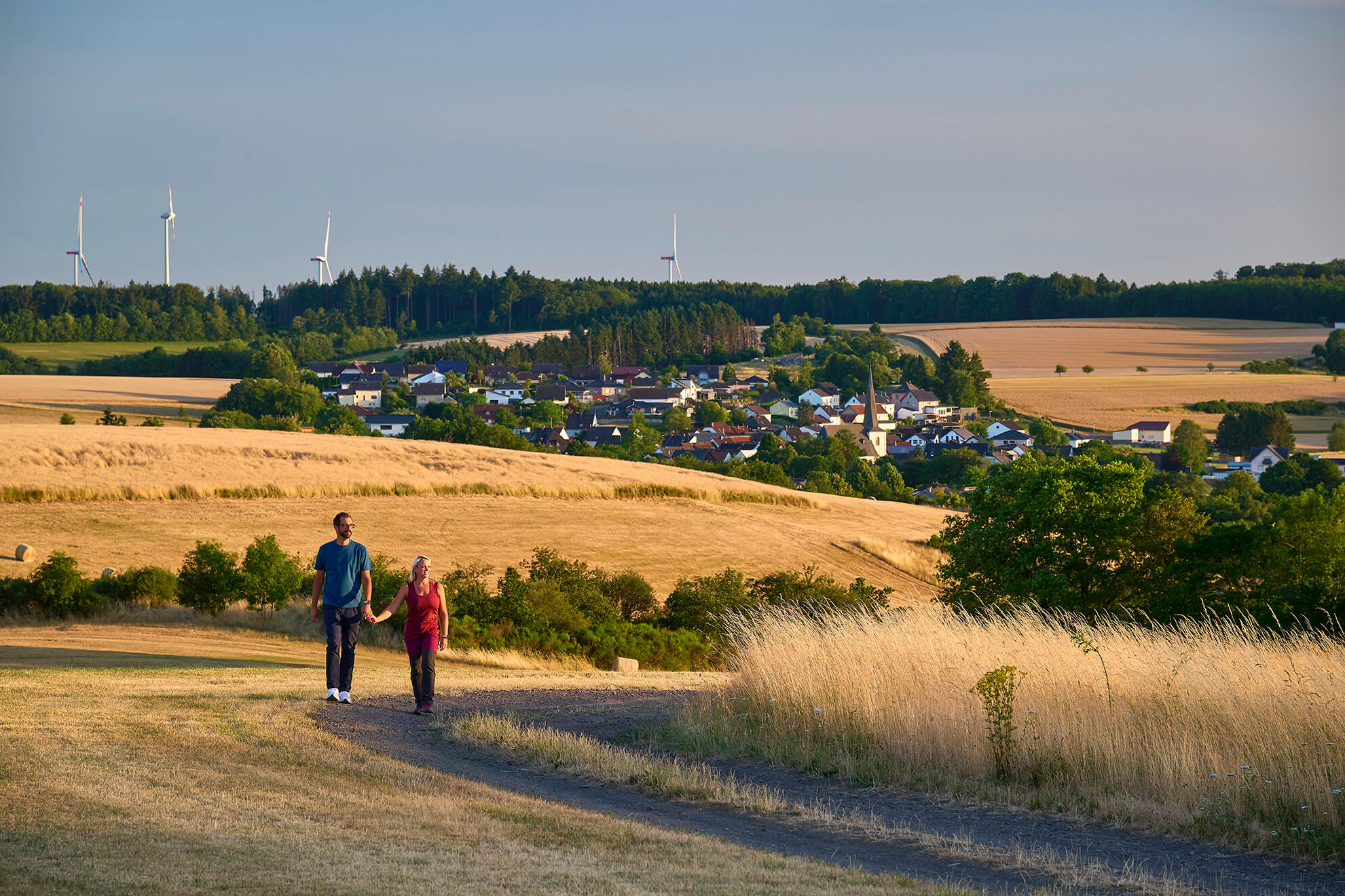 Wanderer auf einem Feldweg mit Blick auf Strohn und die Landschaft der Vulkaneifel