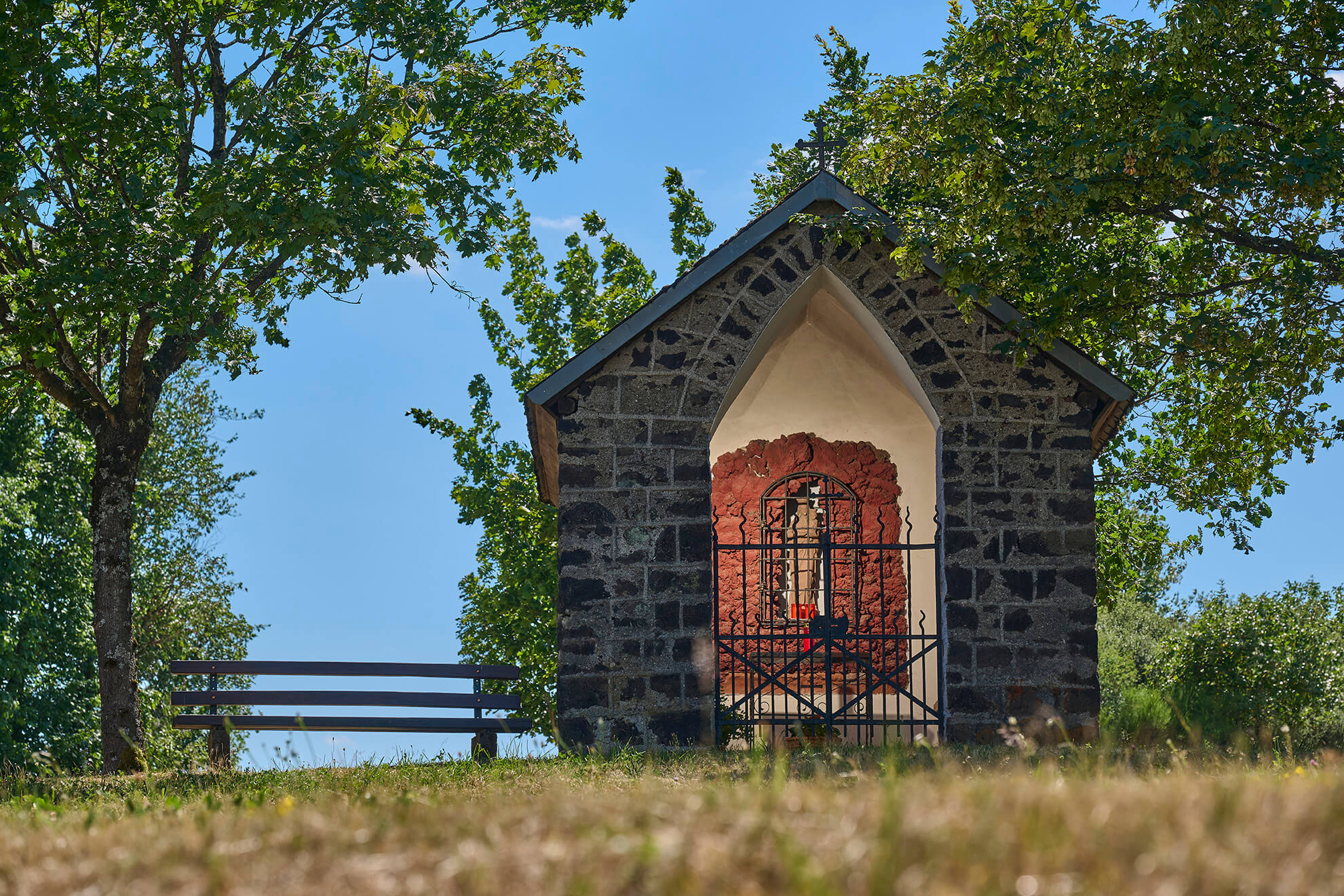 Kleine steinerne Wegekapelle unter Bäumen bei Strohn in der Vulkaneifel